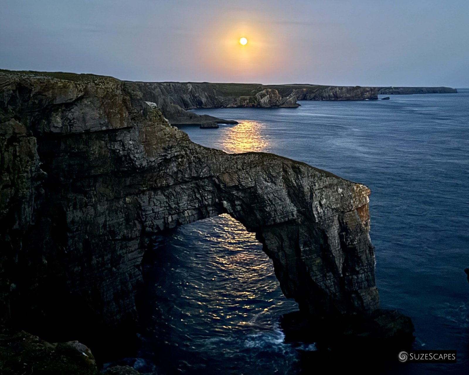 Harvest moon rising at the Green Bridge of Wales, Pembrokeshire, Wales